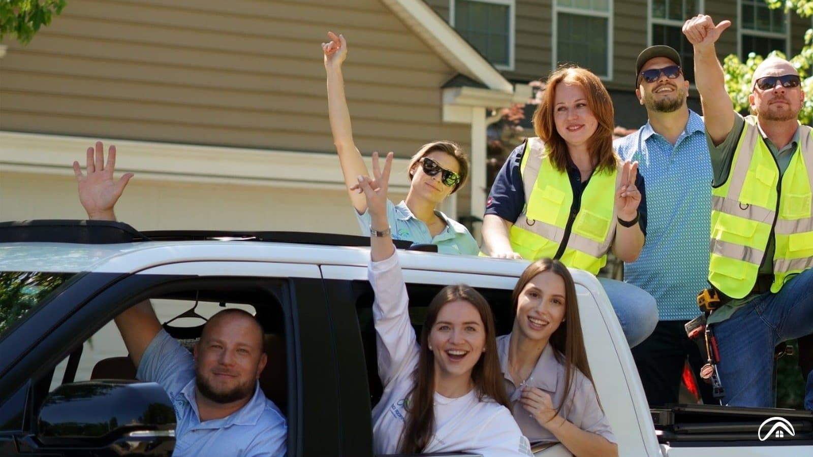 The Good Roofing & Restoration team waving from a white pickup truck in front of a Charlotte home